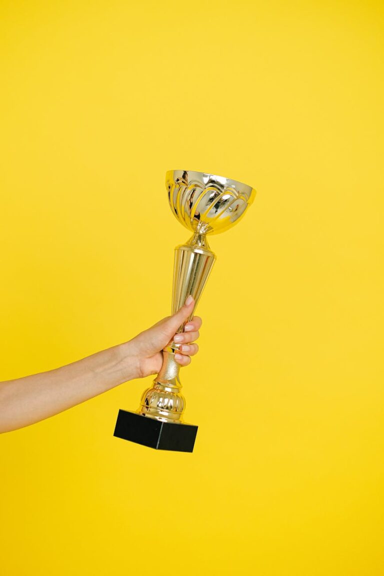 Hand holding a trophy symbolizing achievement and success on a vivid yellow background.
