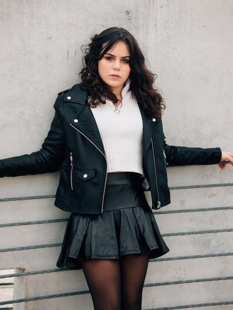 Young woman leaning on fence in stylish black leather jacket, exuding confidence.