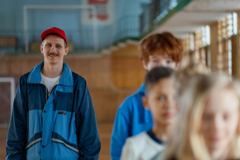 Smiling male coach guiding children in a gym setting during a physical education class.