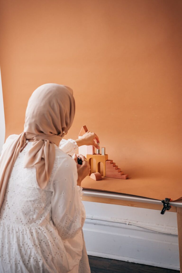 Muslim woman photographing cosmetic products in a studio setup with wooden props.