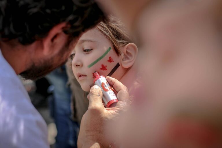 A man paints a child's face with flag colors, creating a symbol of expression.