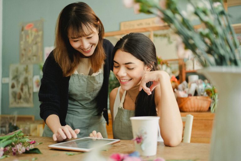 Two cheerful florists in aprons use a tablet while working in a bright floral shop.