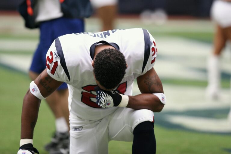 Football player in uniform kneeling before a game, displaying focus and determination.