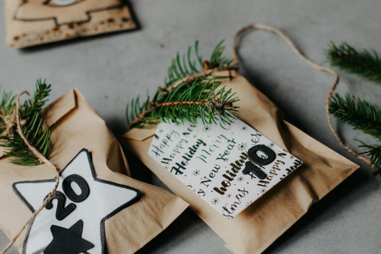 Decorative Christmas gift bags with evergreen sprigs on a gray background, top view.