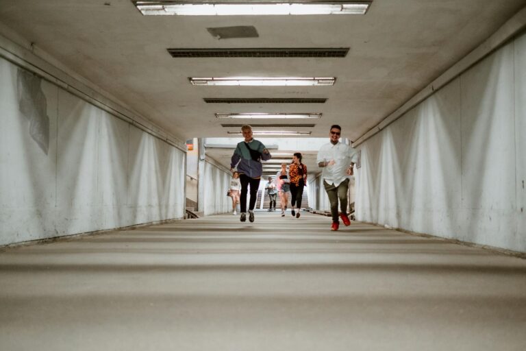 A group of diverse adults happily running together through an urban underpass corridor.