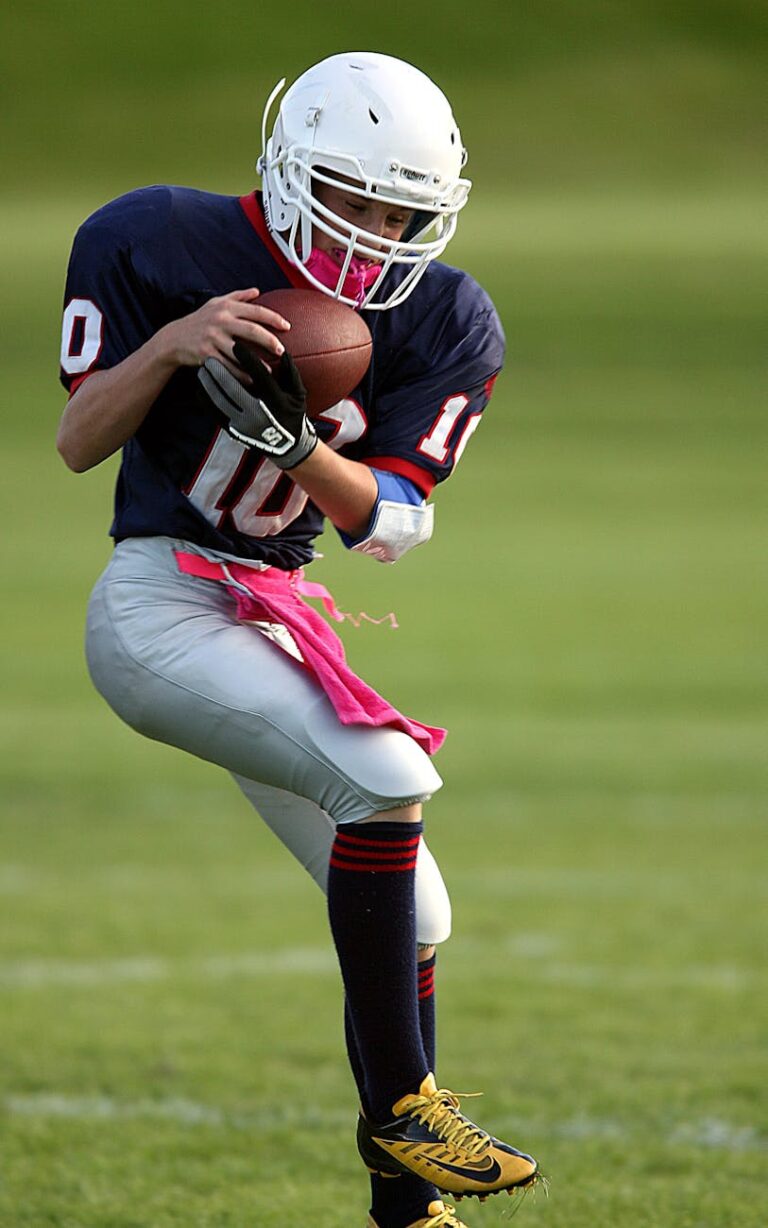 Youth football player catching a pass during a game on a grassy field, showcasing athletic skill.