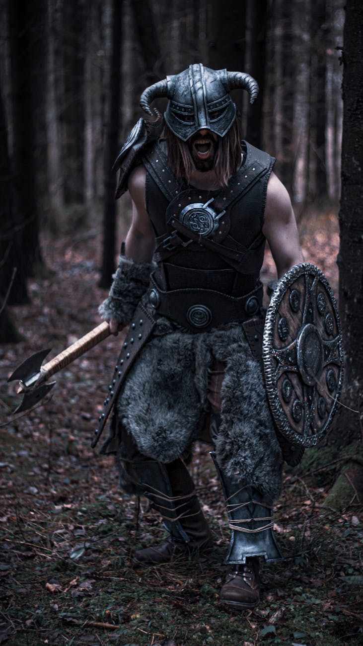A fierce Viking warrior in detailed armor, holding an axe and shield, standing in a dense forest.