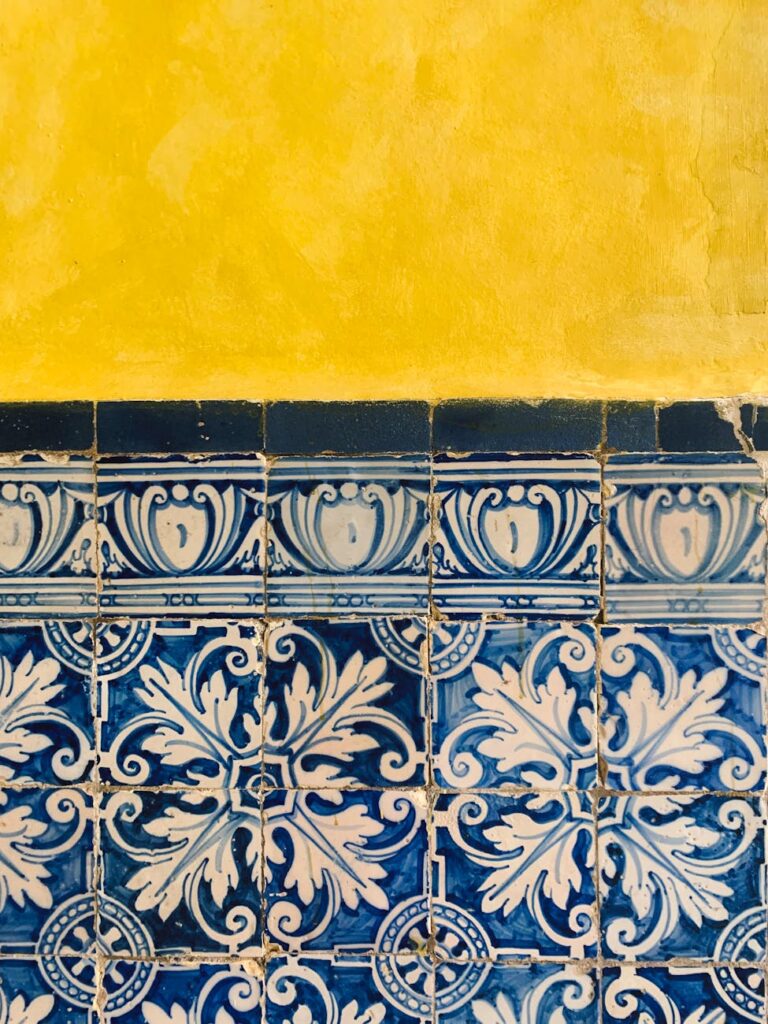 Close-up of intricate blue and white tiles with classic floral motifs beneath a vivid yellow wall.