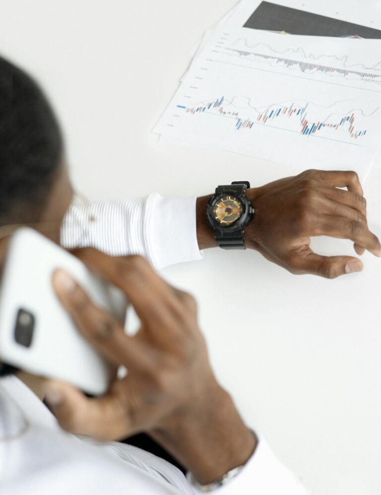 Man examining financial charts on paper while talking on smartphone in office setting.