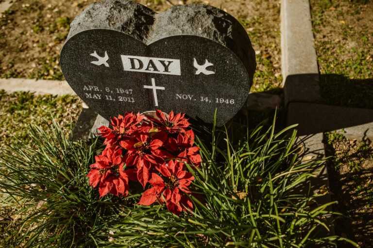 Heart-shaped gravestone with bright red flowers in a peaceful cemetery setting.