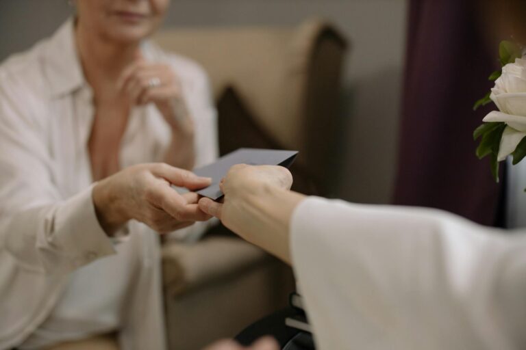 Close-up photograph of two adults exchanging an envelope indoors, conveying communication and warmth.