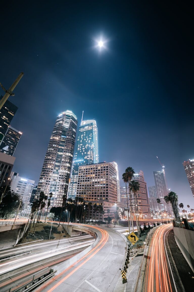 Long exposure of Los Angeles with skyscrapers and light trails under a full moon, capturing urban nightlife.