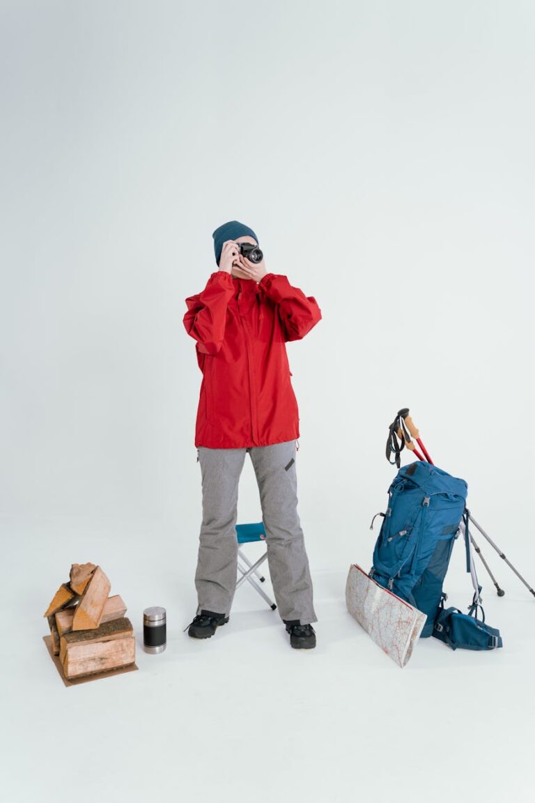 Woman in winter clothing preparing for hiking with backpack and camera, standing indoors.