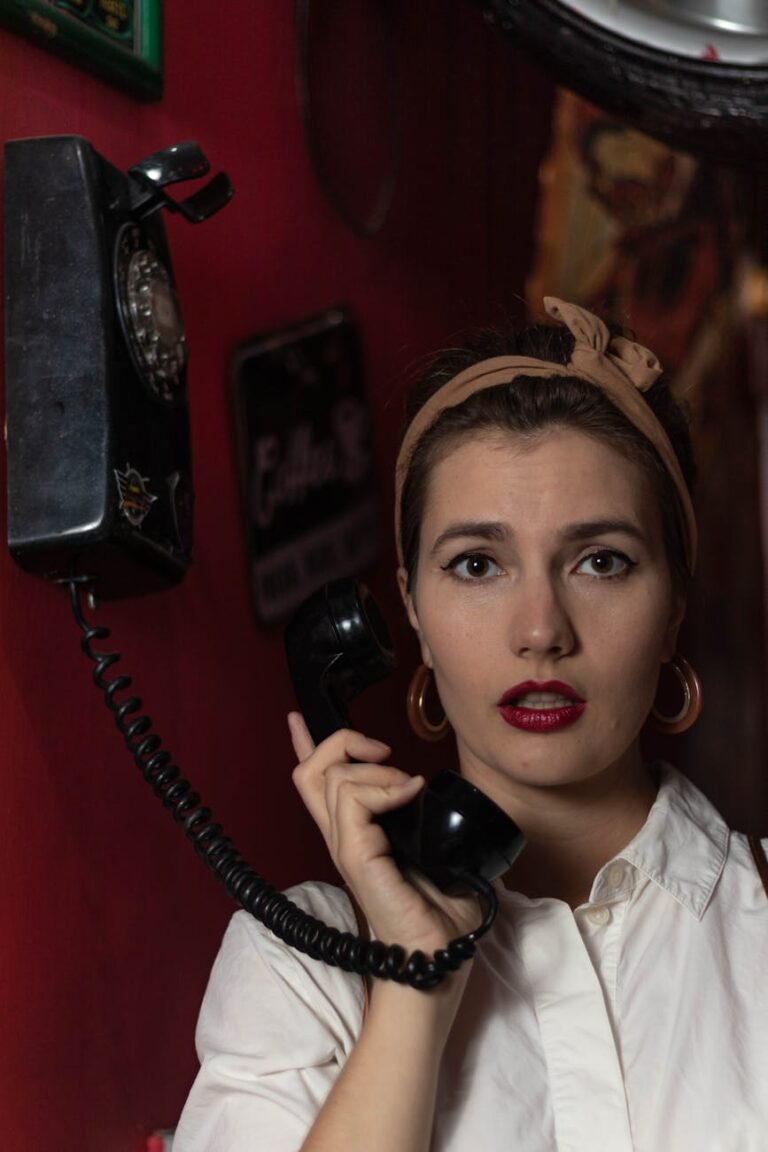 A surprised woman holds an old rotary phone against a vintage red background.