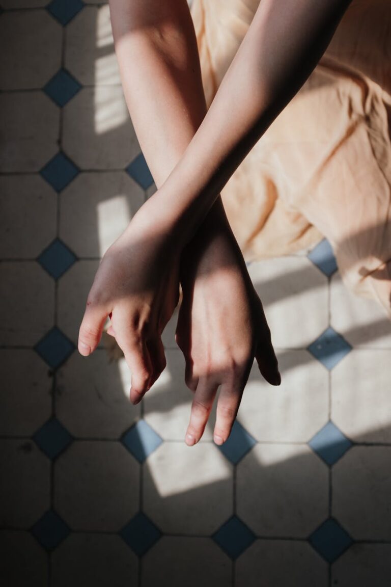 Artistic shot of crossed arms casting shadows on patterned floor, with natural light enhancing elegance.