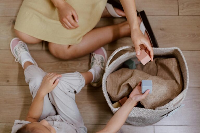 A mother and daughter playing with building blocks on a wooden floor, captured from above.