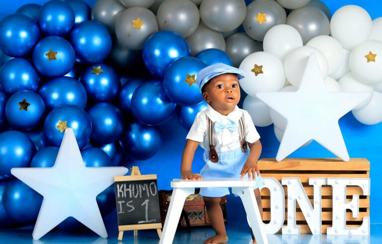 Cute baby celebrating first birthday with blue balloon decor and star theme.