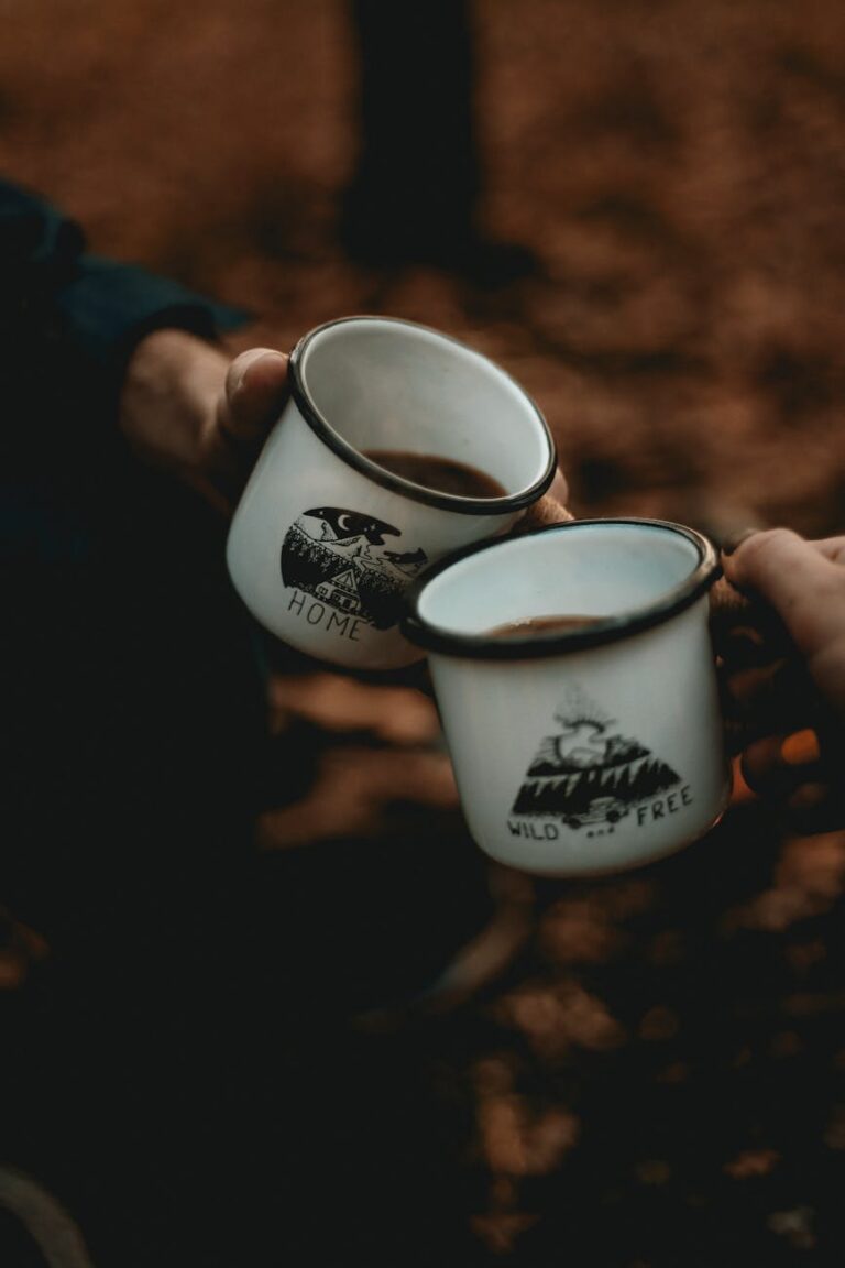 Two people toasting with enamel mugs around a campfire in a forest, creating a warm and adventurous vibe.