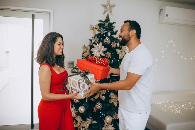 A happy couple exchanging gifts by a beautifully decorated Christmas tree indoors.