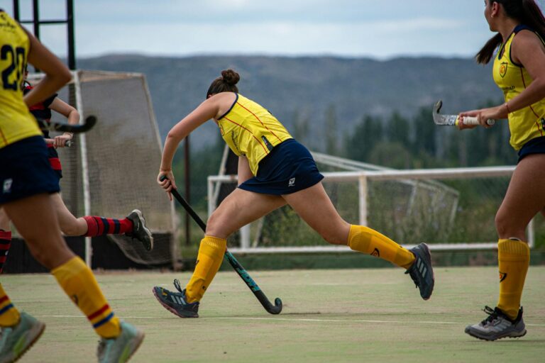 Action shot of a women's field hockey match outdoors, showcasing athleticism and teamwork.