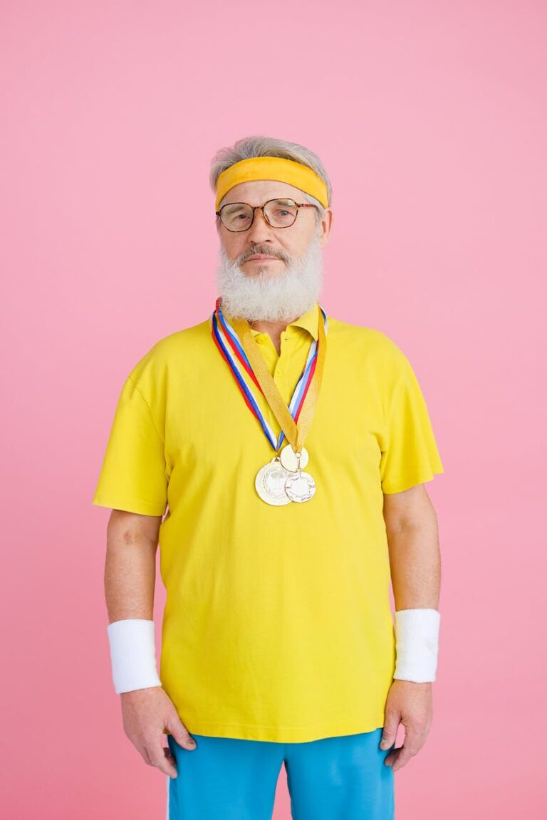 Elderly man in activewear with medals on pink background.