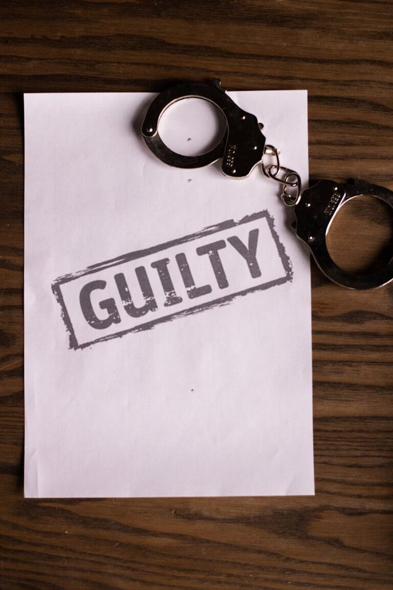 A close-up of handcuffs and a 'Guilty' stamped document on a wooden table, symbolizing law and justice.