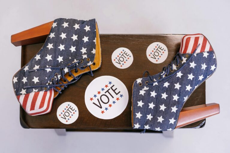 High heel shoes with stars and stripes, surrounded by voting campaign stickers on a wooden surface.