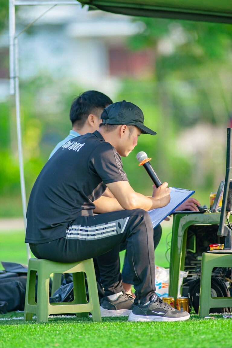 Two men managing a sports event in Hanoi, using a microphone and laptop outdoors.