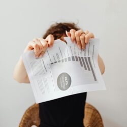 A frustrated individual tearing a printed document with graphs and text.