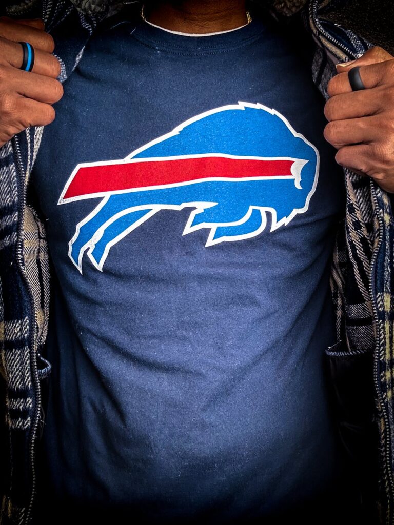 Close-up of person revealing a Buffalo Bills T-shirt in dramatic lighting, emphasizing football fan gear.