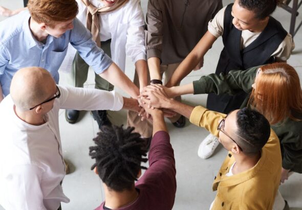 A diverse group of professionals joins hands in a team-building exercise indoors.
