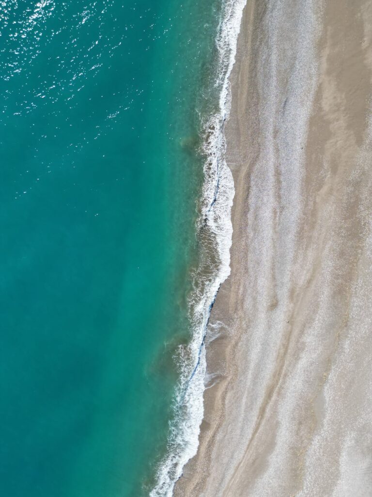 A stunning aerial shot of a turquoise sea meeting a sandy beach in Demre, Antalya, Türkiye.