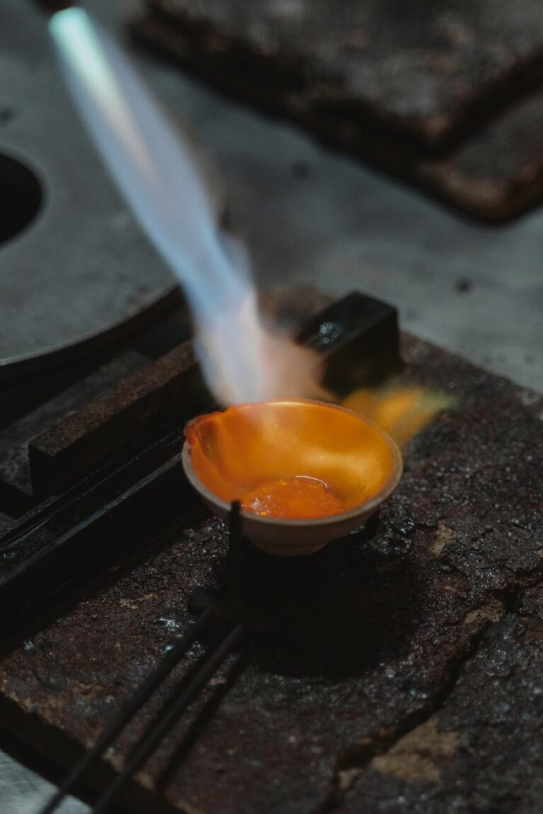 A close-up of metal melting in a dish with a torch flame, highlighting the intense heat and process.