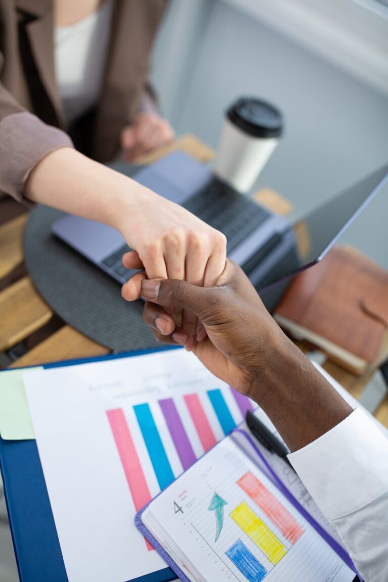 Two professionals seal a business deal with a handshake over a desk with reports.