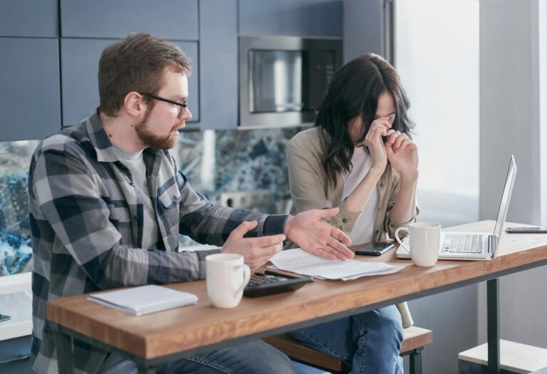A couple sitting at a table indoors, visibly stressed while discussing bills and finances.