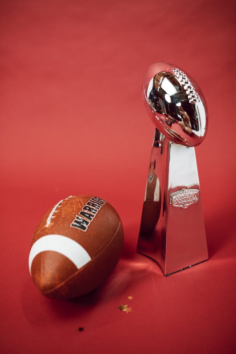 Football and silver trophy on red backdrop symbolizing victory and achievement.