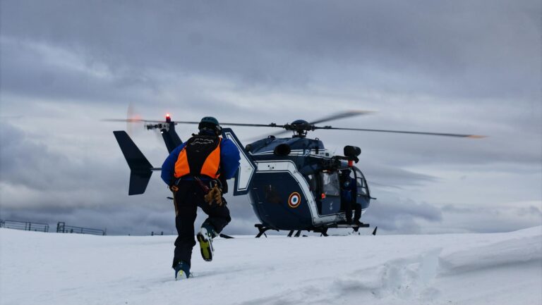 Rescue worker approaches helicopter on snowy field for emergency response.