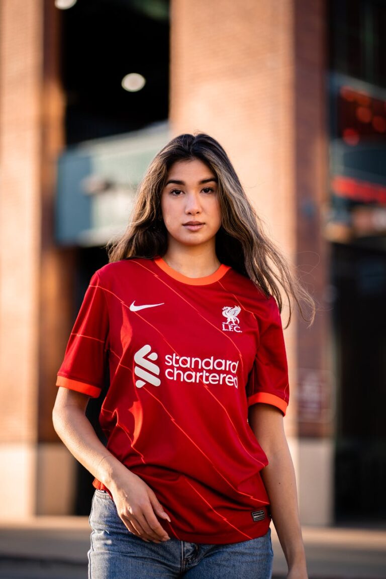 Portrait of a young woman posing confidently in a Liverpool FC shirt outdoors.