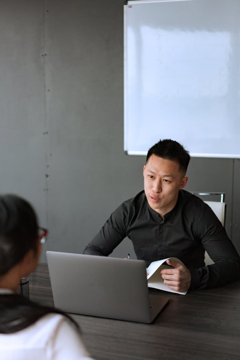 An adult Asian man engaged in a business meeting with a laptop and notes in an office setting.