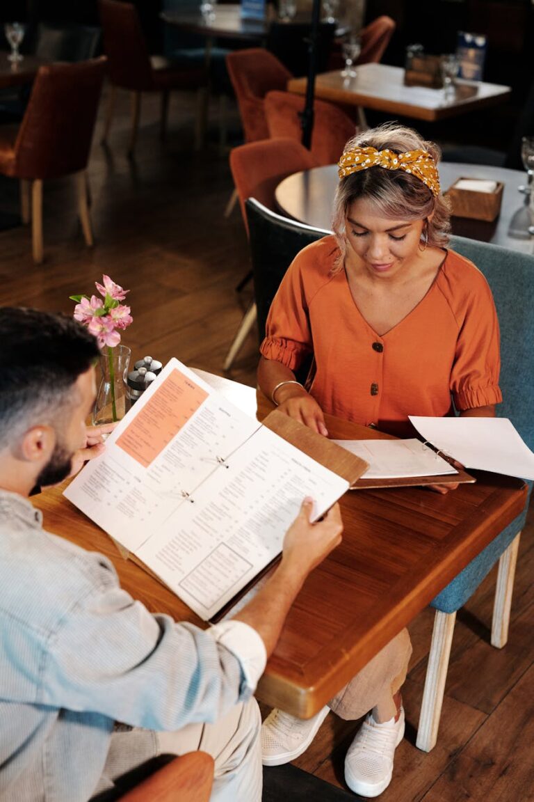 A couple reviews menus while dining indoors at a cozy restaurant, engaging in conversation.