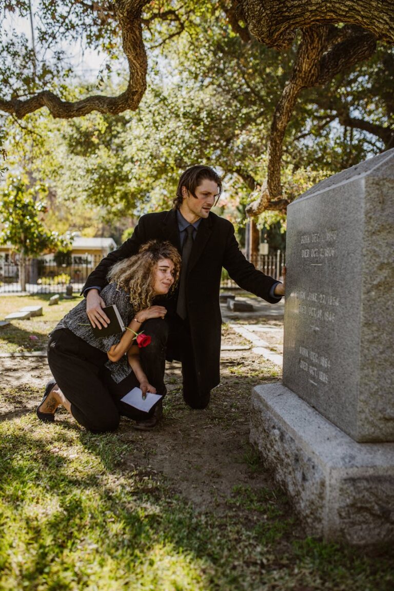 A couple mourns at a grave in a sunlit cemetery, embodying grief and togetherness.