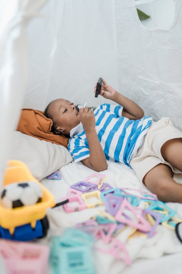 Child lying on a bed playing with colorful toys in a homemade tent indoors.