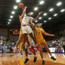 Dynamic basketball game with athletes jumping for the ball during an indoor match.