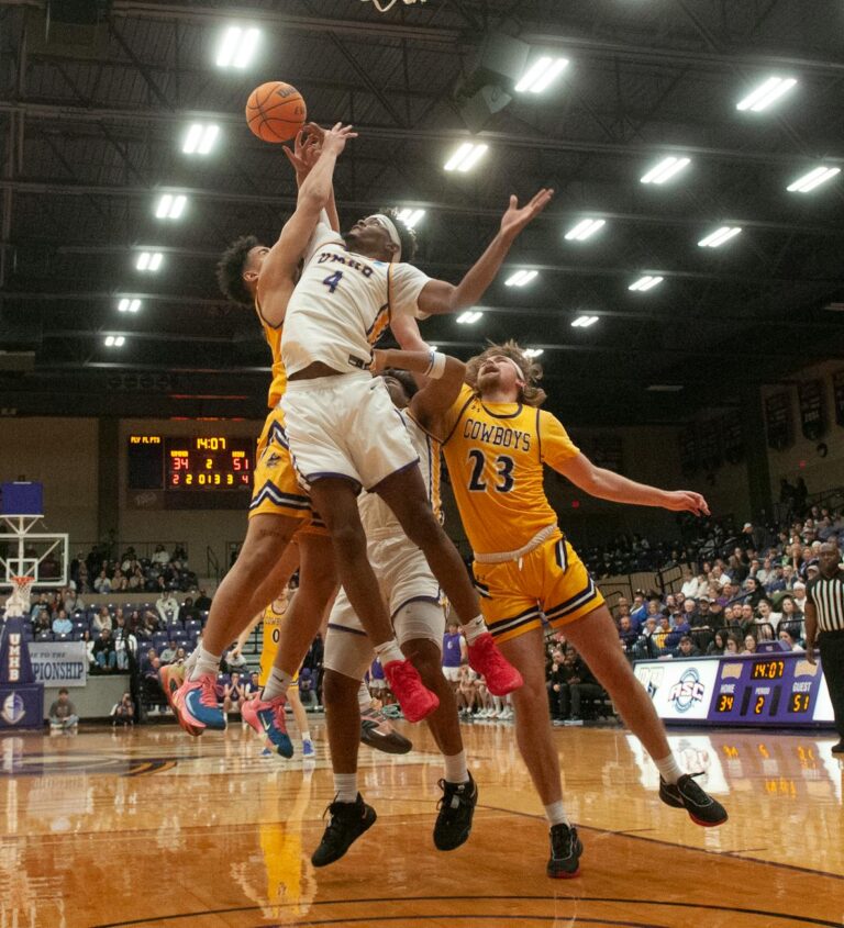 Dynamic basketball game with athletes jumping for the ball during an indoor match.