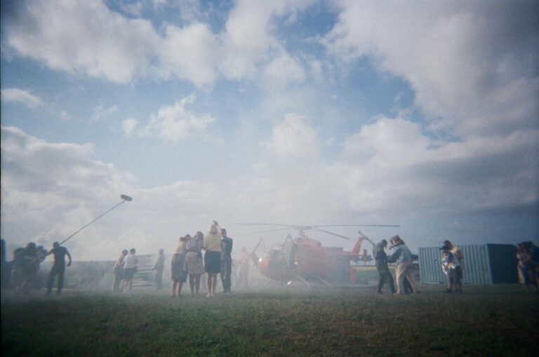 A group of people records a helicopter landing amidst a cloudy sky with equipment.