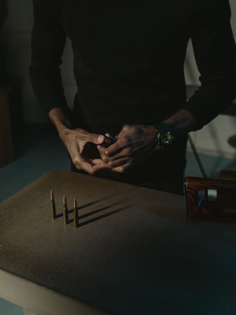 Close-up of a person handling rifle ammunition indoors, emphasizing firearms and security theme.