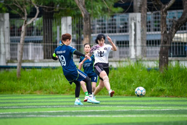 Women energetically playing football on a vibrant field in Hanoi, showcasing teamwork and athleticism.