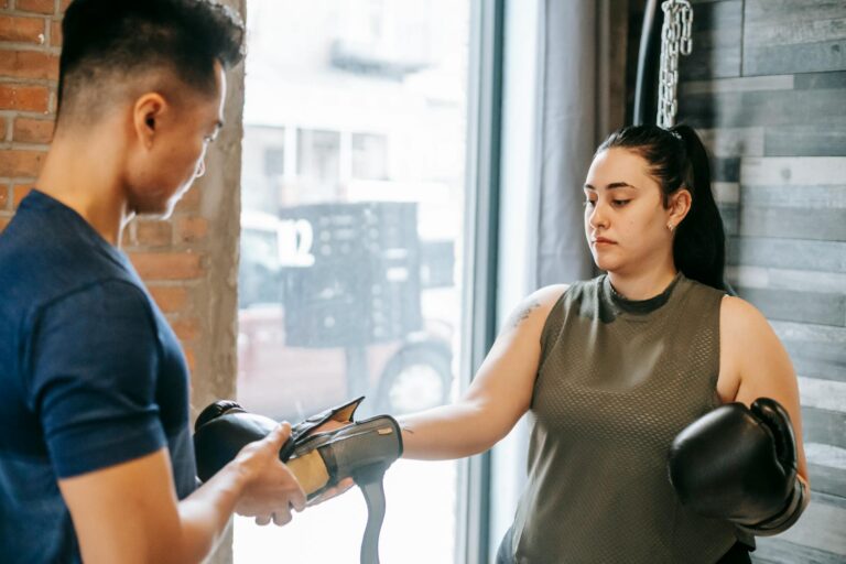 Professional personal trainer preparing focused woman for boxing training while putting on gloves in gym