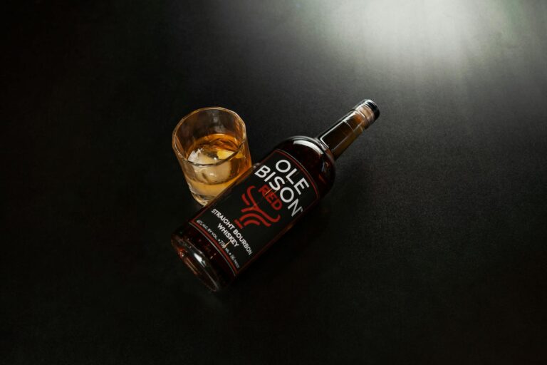 A bottle of Ole Bison Straight Bourbon Whiskey with a glass on a dark surface, New Orleans.