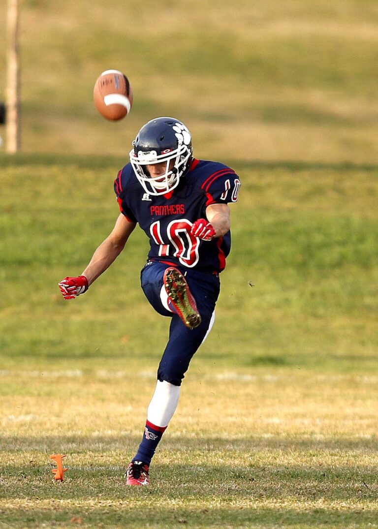 Dynamic action shot of an American football player kicking the ball on a grassy field.